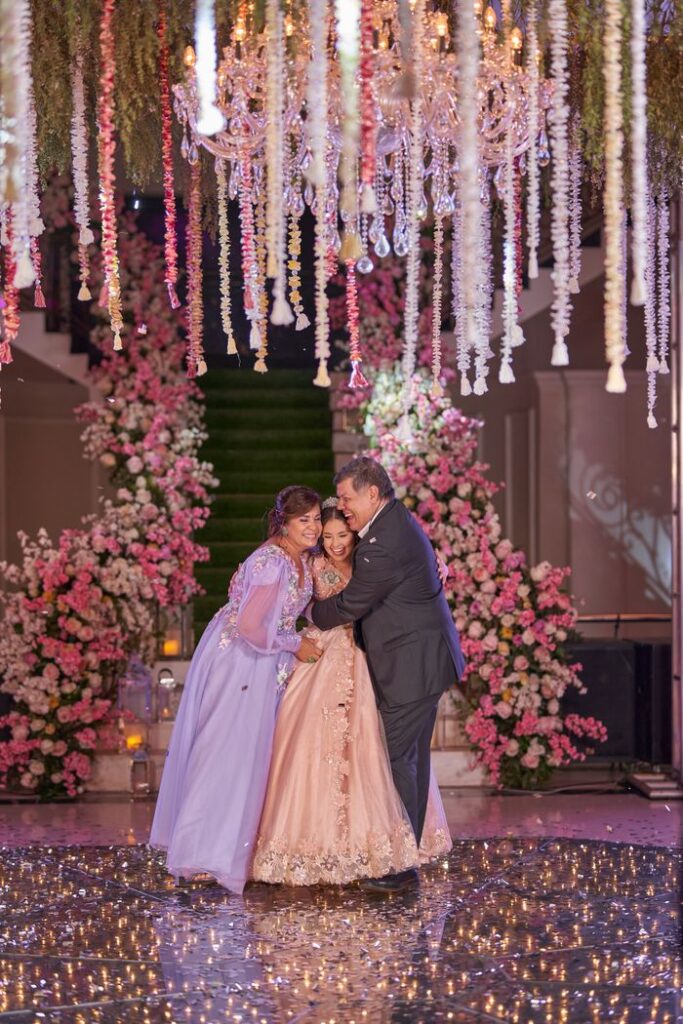 A joyful quinceañera celebration featuring a teenage girl with her well-dressed parents in an elaborately decorated hall.