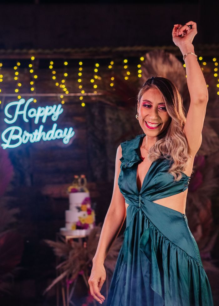 A joyful birthday celebration with a woman smiling and raising her hand inside a decorated venue.