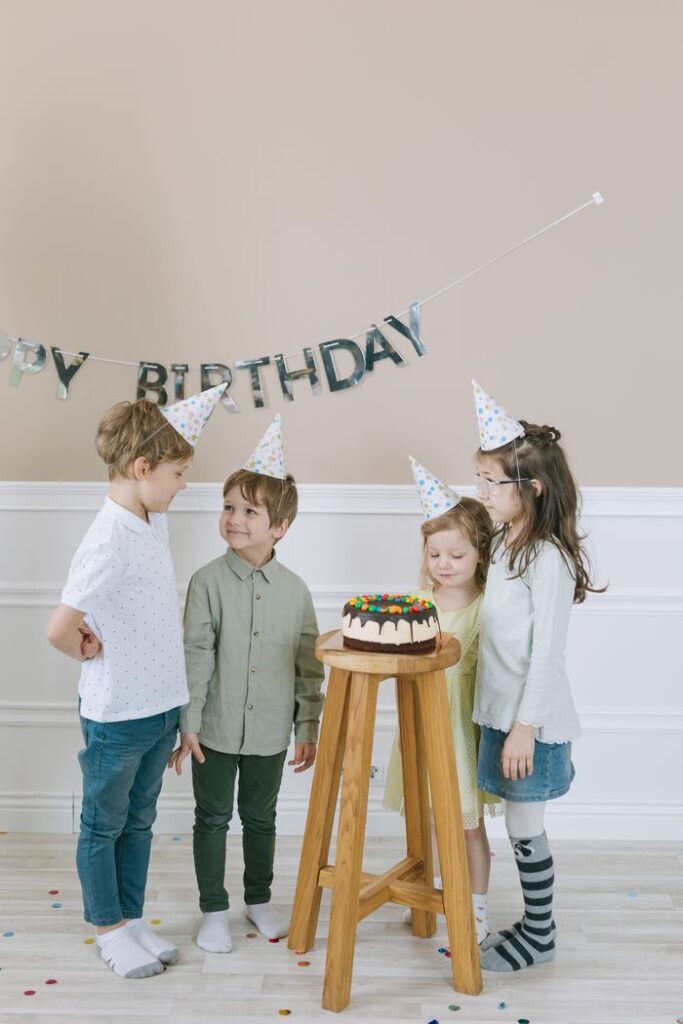 Group of kids celebrating birthday with cake and party hats, indoors.